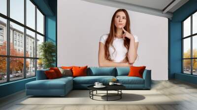 Portrait of standing with thoughtful serious smart expression, pondering answer, having doubts and suspicion, wearing white T-shirt. Indoor studio shot isolated on gray background. Wall mural