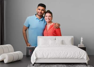 Portrait of young attractive family couple in casual wear standing together, embracing and looking at camera with sincere smile, strong relations. isolated on gray background, indoor studio shot Wall mural