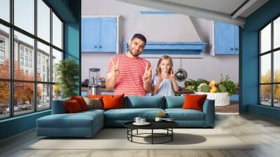 Positive young father and daughter gesturing peace victory or v sign, smiling at camera in kitchen, tablet pc and fresh green vegetables on table behind, recipes from internet, vegetarian nutrition Wall mural