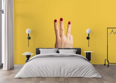 Profile side view closeup of woman hand with red manicure showing number 3 three with hands. Indoor studio shot isolated on yellow background. Wall mural