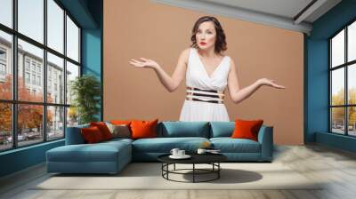 Puzzled middle aged woman say i don't know. Emotional expressing woman in white dress, makeup, red lips and dark curly hairstyle. Studio shot, indoor, isolated on beige or light brown background Wall mural