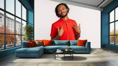 Satisfied bearded man wearing red casual style T-shirt, pointing finger at himself feeling proud and ambitious, boasting successful achievement. Indoor studio shot isolated on gray background. Wall mural