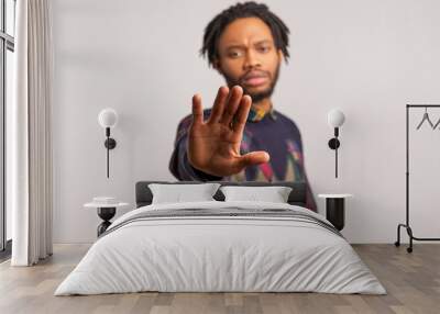 Worried african man with dreadlocks showing stop gesture with palm of his hand, concerned about bullying and domestic violence, need help. Indoor studio shot isolated on gray background Wall mural