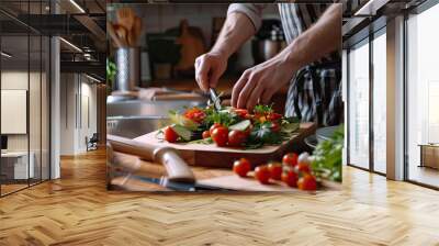 A man in a home kitchen focuses on cutting vegetables for a fresh salad on a wooden chopping board. Wall mural