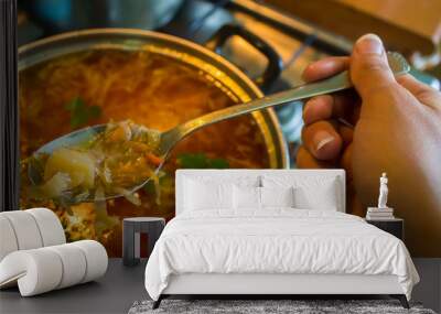 Hand with spoon of soup in kitchen Wall mural