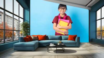 Graduate and education concept, Asia Thai girl kid student holding books and earphone on blue background in studio Wall mural