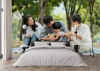 Happy family with grandma, mom with dad teaching son  playing guitar and sing a song in park, Enjoy and relax people picnic outside Wall mural