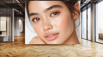 A close-up portrait of a young woman with flawless, dewy skin and minimal makeup. She gazes softly at the camera, with her hand gently resting on her chin, set against a white background Wall mural