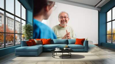 Asian caregiver talking senior male patient checkup in living room at home. Older elderly man consults after physical therapy. Nurse assistance rescue concept. Wall mural