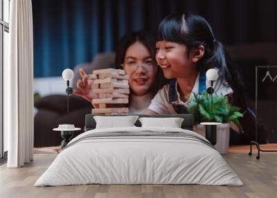 Asian happy family of little daughter play toy wooden block in home. Mother or mom young woman loving parent having fun play stack tower wood block game at night in living room. Hobbie leisure concept Wall mural