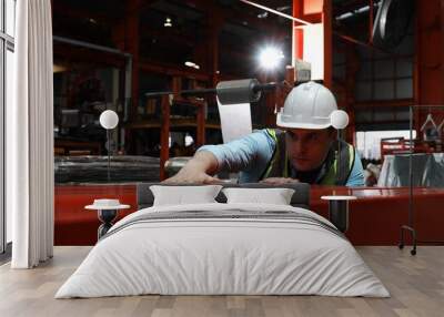 Engineer man wearing green uniform and safety white helmet under inspection and checking production process on factory station. Warehouse workshop for factory operators at metal industry factory. Wall mural