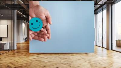 Hands holding blue happy smile face, good feedback rating, positive customer review, experience, satisfaction survey, smiley mental health, child wellness, world mental health day on blue background Wall mural