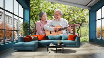 Happy Asian senior couple elderly man playing guitar music song enjoy having fun happiness outside house near backyard garden. Retirement insurance concept Wall mural