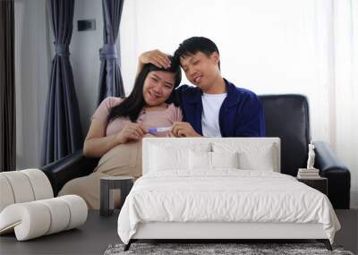 Happy man with pregnant wife rubbing his belly while relaxing and spending time in modern apartment. Pregnant woman and husband spending time together using smartphone Wall mural