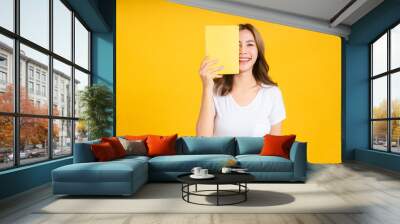 Portrait young happy asian woman book covering your eye reading education studying learning knowledge smiling positive emotion in white t-shirt, Yellow background isolated studio shot and copy space. Wall mural