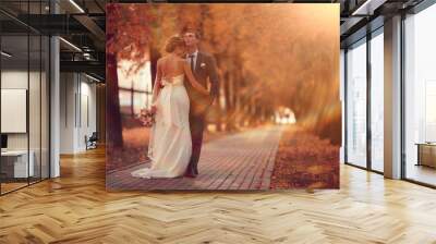 Newlyweds groom and bride walking in autumn park Wall mural