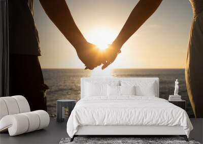 Couple bride and groom holding hands at sunset facing the ocean. Love and relationships concept.  Wall mural