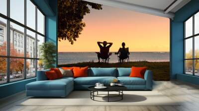 Couple relaxing together sitting on a beach chair enjoying the sunset nature view Wall mural