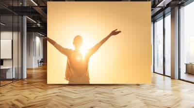 Feelings of hope light. Female lifting her arms up to the golden sky  Wall mural