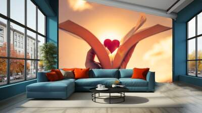 Hand holding book, bible up to the sunlight with silhouette of heart. Faith hope and love concept. Religious belief symbol.  Wall mural