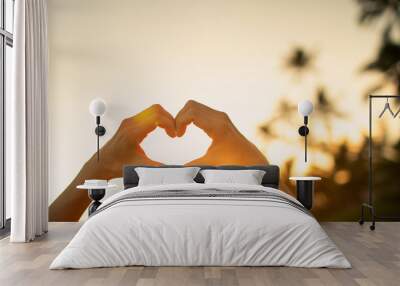 Hand making heart shape on beautiful sunset background.  Wall mural