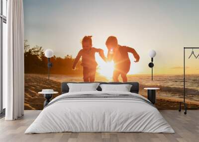 Happy little boy and girl kids playing jumping for joy on the beach having summertime fun  Wall mural