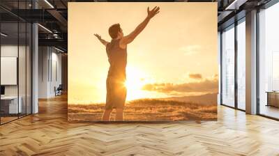 Happy man looking up to the sky with arms raised up to the sunset.  Wall mural