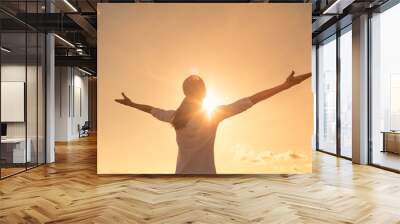 Happy positive woman looking up to the sunset sky with arms up feeling free Wall mural