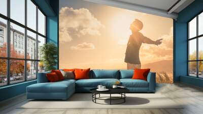 It's a beautiful life! Young man with arms up to the sunlight standing in a meadow field. Wall mural