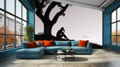 Man praying. Religion concept. Young man with his hands folded together sitting under a tree.  Wall mural