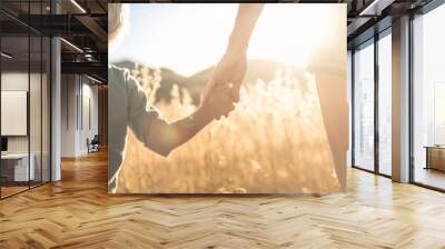 Mother little child holding hands walking in a grass field at sunset.    Wall mural