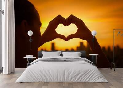 Silhouette of girl holding up heart against a beautiful sunset. Giving and love in the city concept.  Wall mural