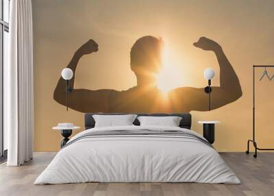 Strong fit man flexing against sunset sky. People power and winning concept.  Wall mural