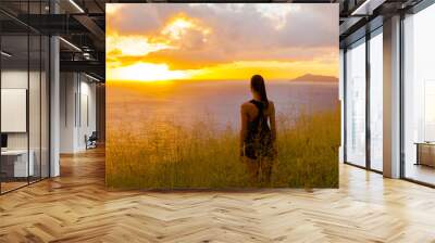 Young female standing on a hill looking down at the beautiful sunset.  Wall mural