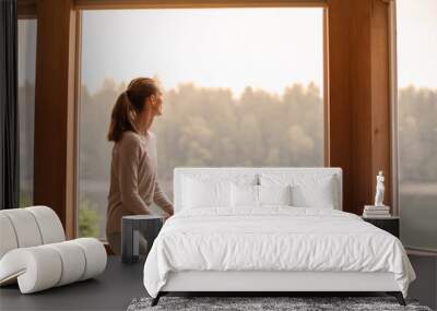 Young woman looking out window early morning  Wall mural