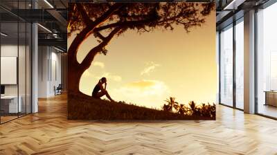 Young woman siting under a tree enjoying the beautiful golden sunset.  Wall mural