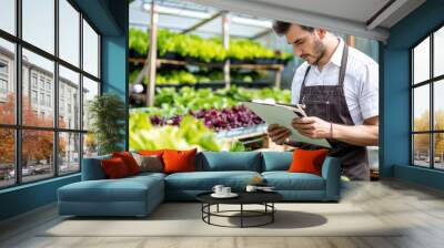 A farmer writing notes in his notebook while standing among greenery growing inside a greenhouse Wall mural