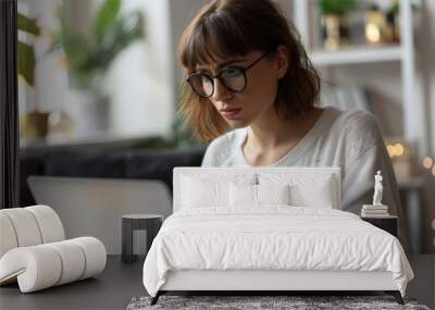 a woman in an office holding a credit card and looking at a laptop while sitting on a desk with a worried expression Wall mural