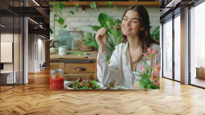 A young woman is sitting at a table eating salad, smiling happily with her eyes closed in front of you Wall mural