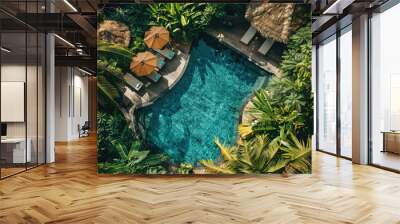 An aerial view of the pool and loungers at a luxury hotel in Bali, surrounded by lush greenery. The oval shaped pool has two sunshades over it, surrounded by palm trees and other tropical plants. Wall mural