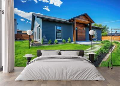 Modern home with a gray and blue exterior, a green grass lawn, a wooden fence, a clear sky, and a blue background Wall mural