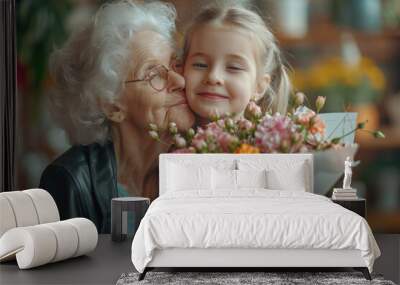 Portrait of cute little girl embracing and kissing her grandmother in cheek giving bunch of flowers and postcard, greeting woman with holiday, Women's or Mother's Day Wall mural