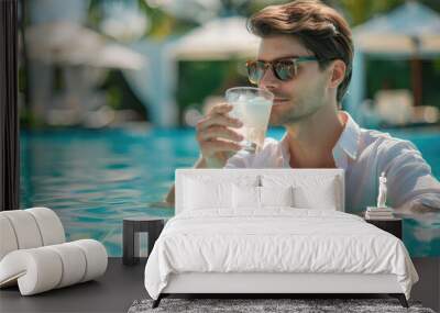 Young man hotel guest sipping a cocktail in the outdoor hotel swimming pool during summer holidays Wall mural