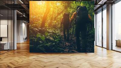 A serene scene of two hikers exploring a lush green forest at sunset, surrounded by towering trees and vibrant foliage. Wall mural