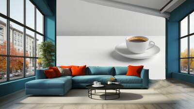 A white coffee cup sits on a white plate on a white table. The cup is filled with coffee and has a brown rim. Concept of calm and relaxation, as the simple white table Wall mural