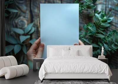 Hands holding a blank white card in a cozy room with plants Wall mural