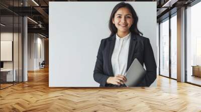 A confident businesswoman in a professional suit, smiling and holding a laptop, standing against a solid white background with ample copy space on either side. Wall mural