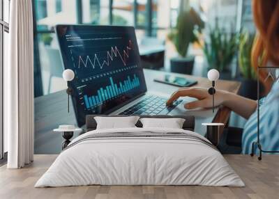 A female accountant working on a laptop in a modern office space, with graphs and charts displayed on the screen.  Wall mural