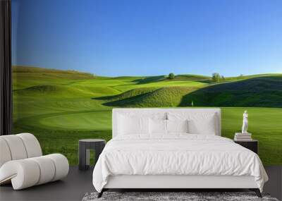 A scenic view of a golf course with rolling hills and a clear blue sky. Wall mural