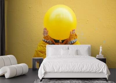 A child in a yellow jacket holds a large yellow balloon against a matching wall. Wall mural